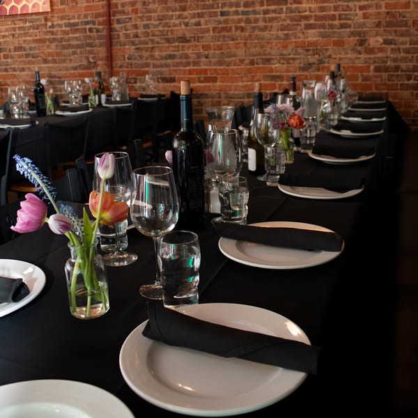 Set tables with black tablecloths, white plates, wine glasses, and small floral arrangements in Honeycomb Cafe.