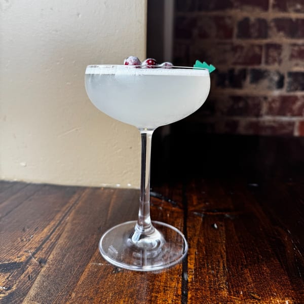 A Honeycomb Cafe cocktail, garnished with berries and a green pick, on a wooden table.