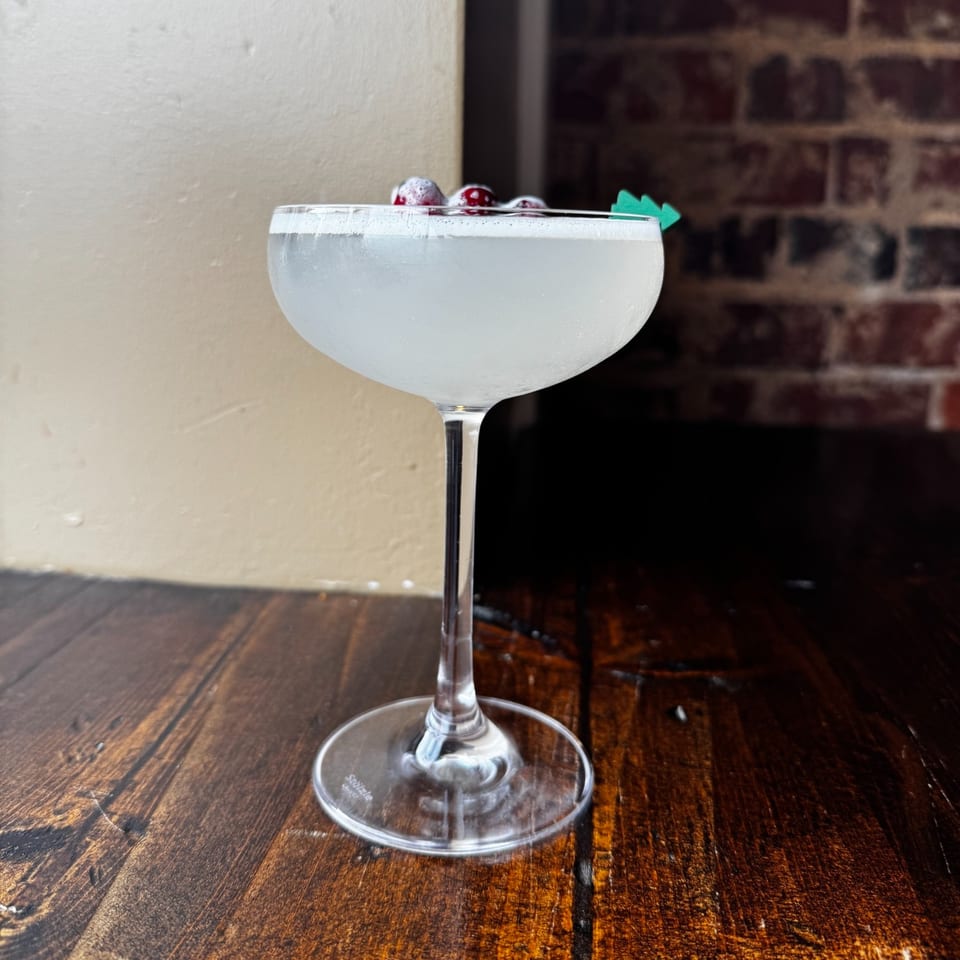 A Honeycomb Cafe cocktail, garnished with berries and a green pick, on a wooden table.