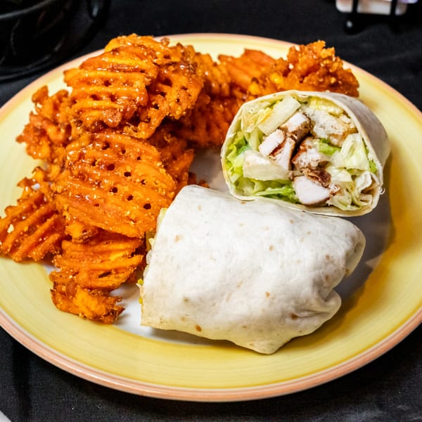 A Honeycomb Cafe chicken wrap with lettuce and sweet potato waffle fries on a yellow plate.