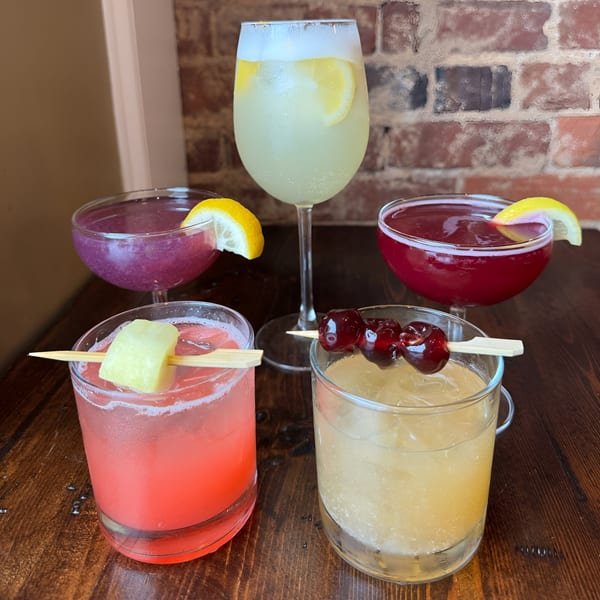 Four colorful Honeycomb Cafe cocktails, two with lemon slices, one with pineapple, and one with cherries.