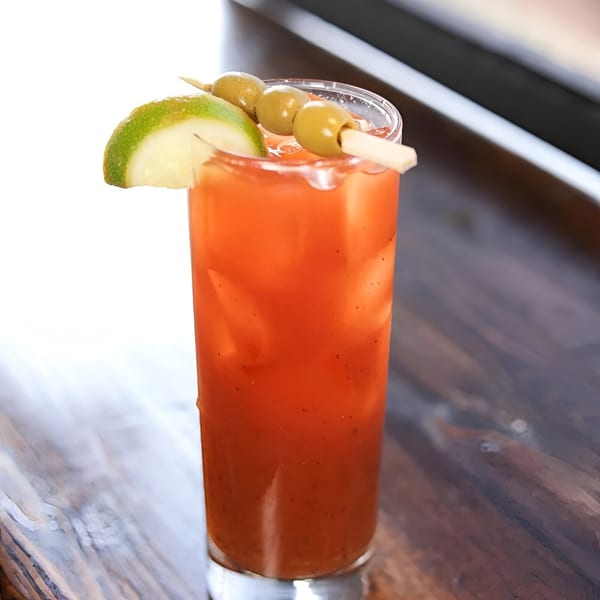 A Honeycomb Cafe Bloody Mary cocktail with lime and olive garnish on a rustic wooden table.
