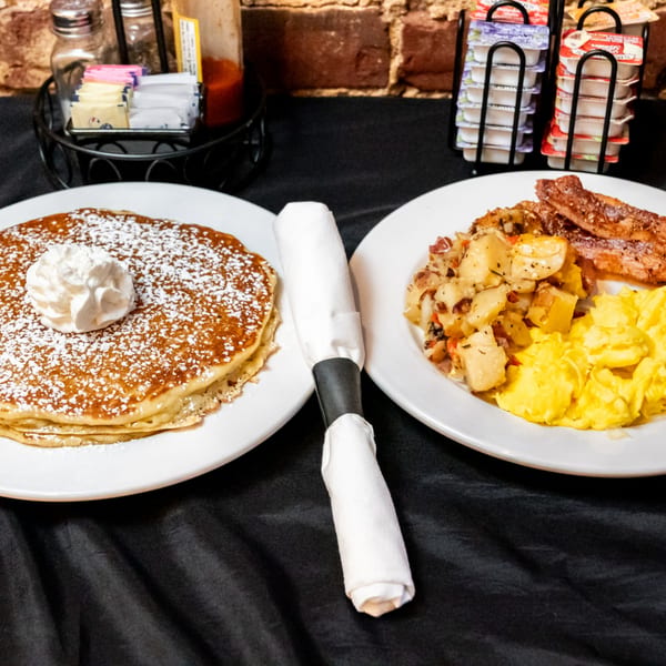 Honeycomb Cafe's pancakes with whipped cream, and a breakfast plate with scrambled eggs, bacon, and potatoes.