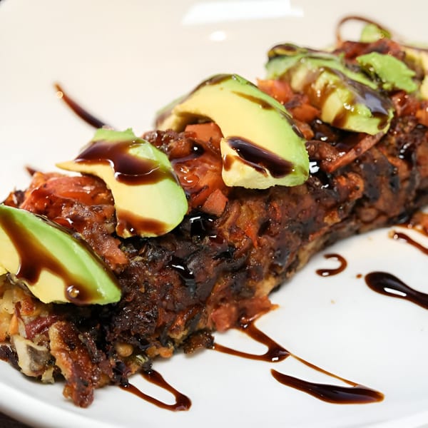 Savory dish topped with sliced avocado, bacon bits, and a dark balsamic glaze on a white plate.