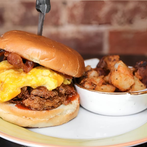 A Honeycomb Cafe breakfast sandwich with scrambled eggs, bacon, and pulled pork, served with home fries.